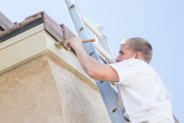 Professional Exterior Painter painting the top side of the roof on a ladder