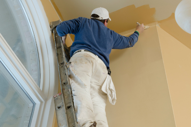 Professional house painter om a ladder with a paint brush painting ceiling