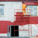 Residential exterior painter on a scaffold with a roller and red paint